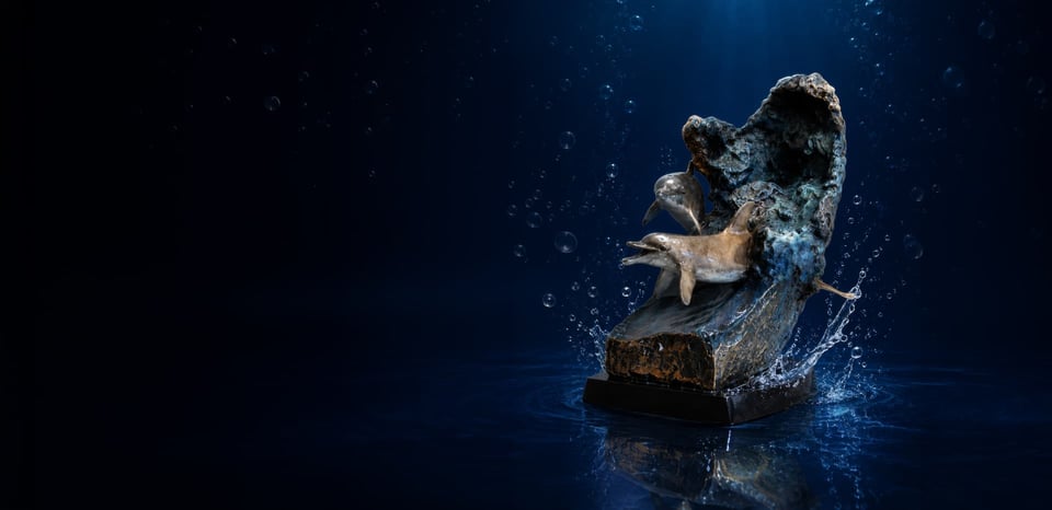 Bronze dolphin memorial sculpture rising from a sculpted wave against a deep blue underwater backdrop