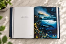 Open book on marble showing the Two Worlds of Paradise plate and Wyland's handwritten quote